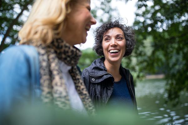 Two women smiling at each other and walking in a park