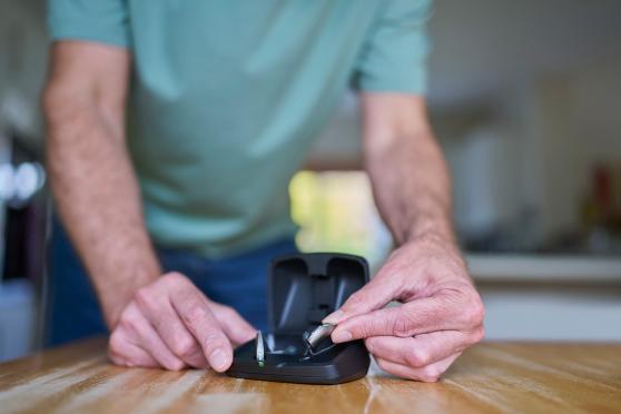 Man holding a case of hearing aids that are sitting on a table